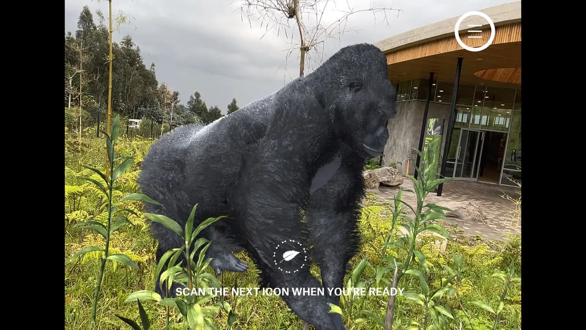 An AR silverback on all fours among tall plants beside the campus building.