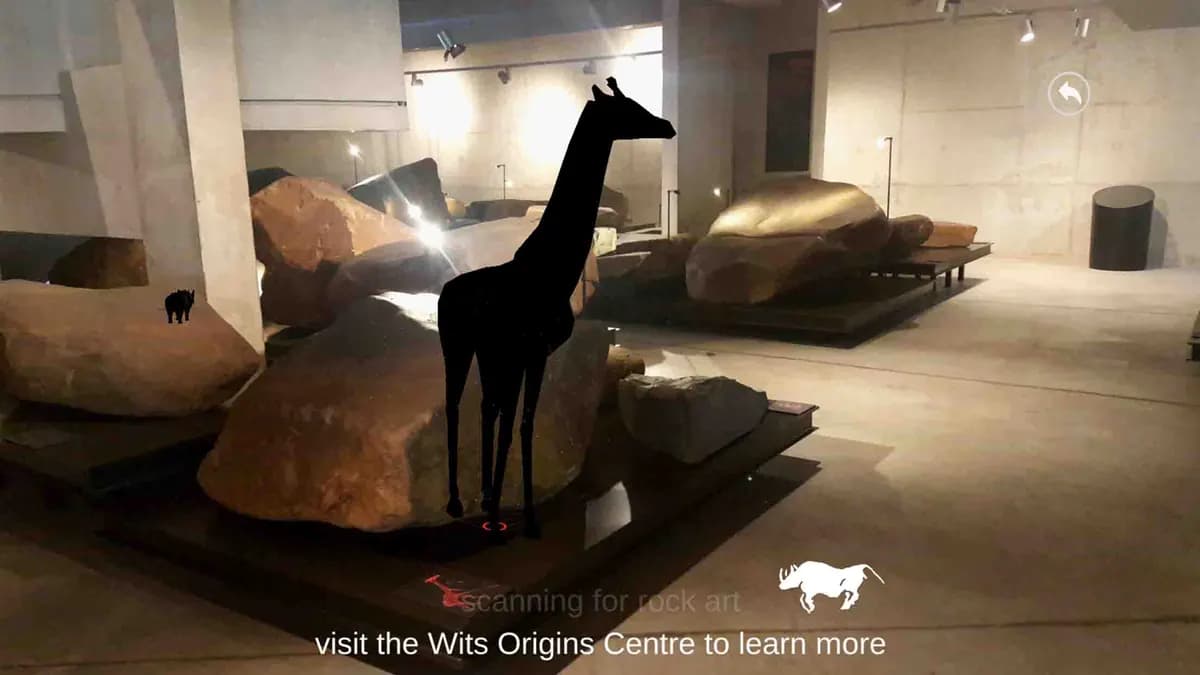 A dark giraffe silhouette stands among engraved rocks in the museum gallery.