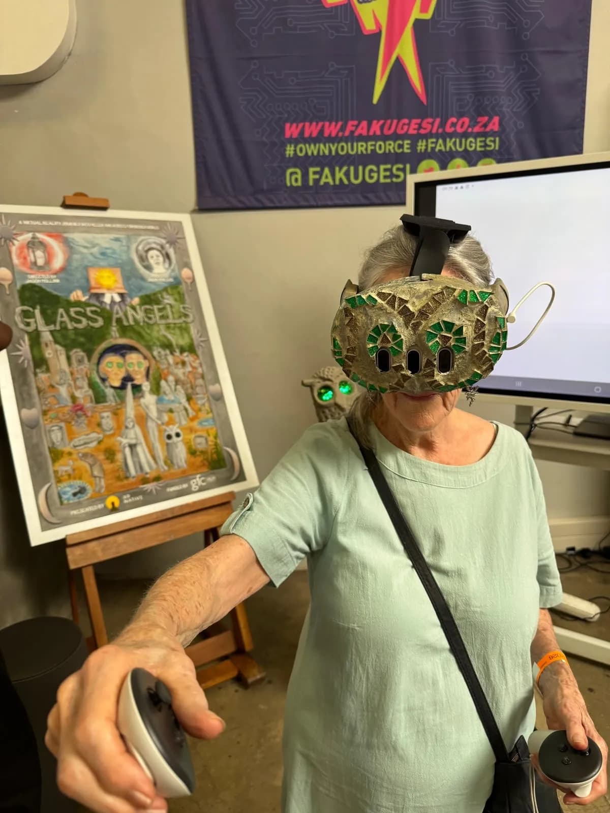 A visitor in the headset reaching forward with a controller, beside the painted Glass Angels poster