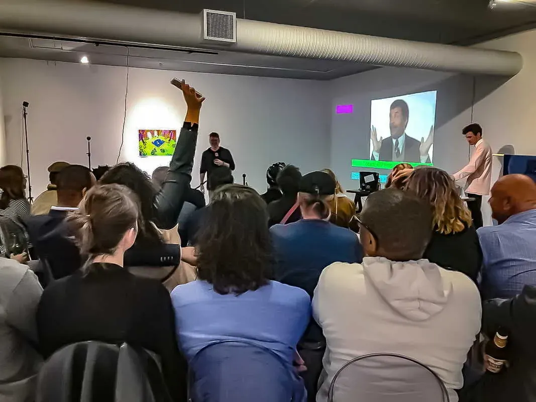 A full room at a WeAReVR Jozi meetup in 2019. Seated guests face a speaker with a mic and a projected video, someone works at a laptop at the side, and one guest has an arm raised.