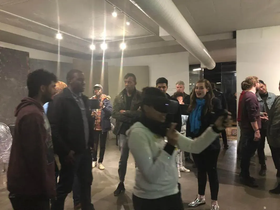 A WeAReVR Jozi meetup in 2019. A visitor in a VR headset reaches out with one hand while a crowd stands around them watching, some of them smiling.