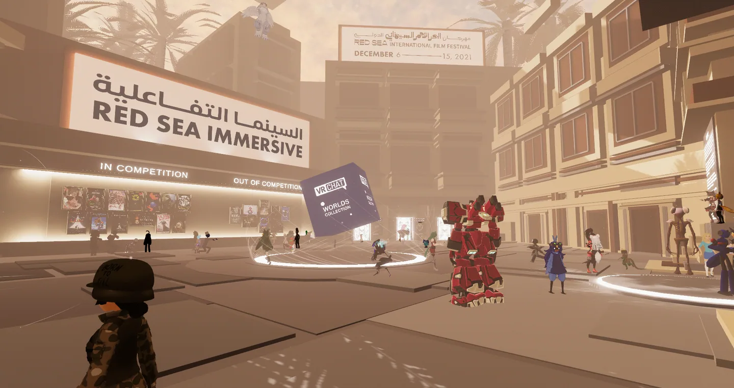 The Red Sea Immersive plaza in VRChat. Avatars mill around a floating "VRChat Worlds Collection" cube, in front of poster walls marked In Competition and Out of Competition, under a festival billboard for 6 to 15 December 2021.